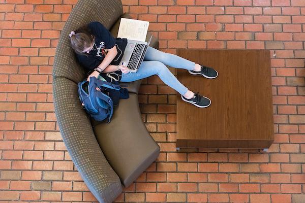 Student sitting on couch with laptop in their lap.